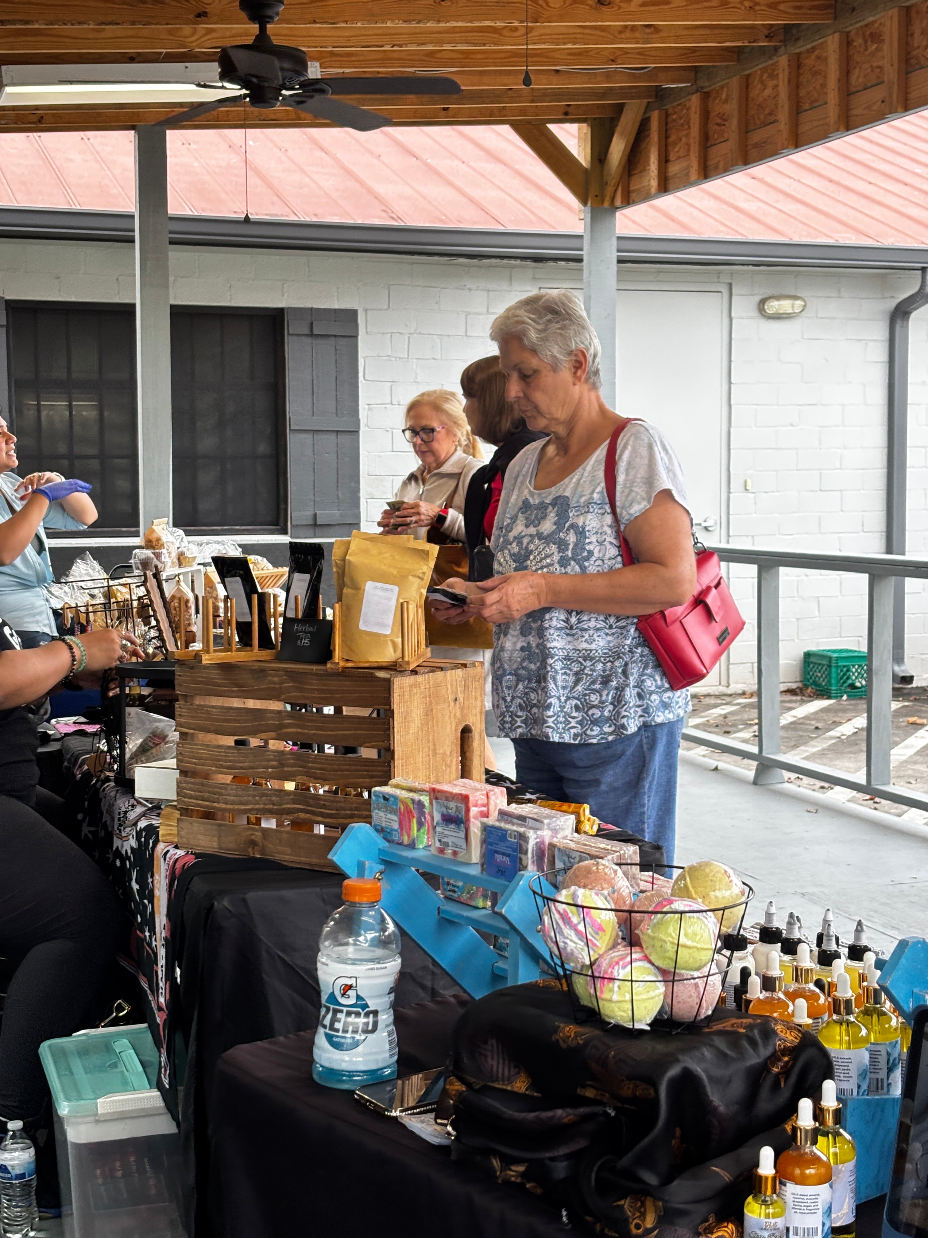 People shopping at an outdoor market with various goods and a building in the background.