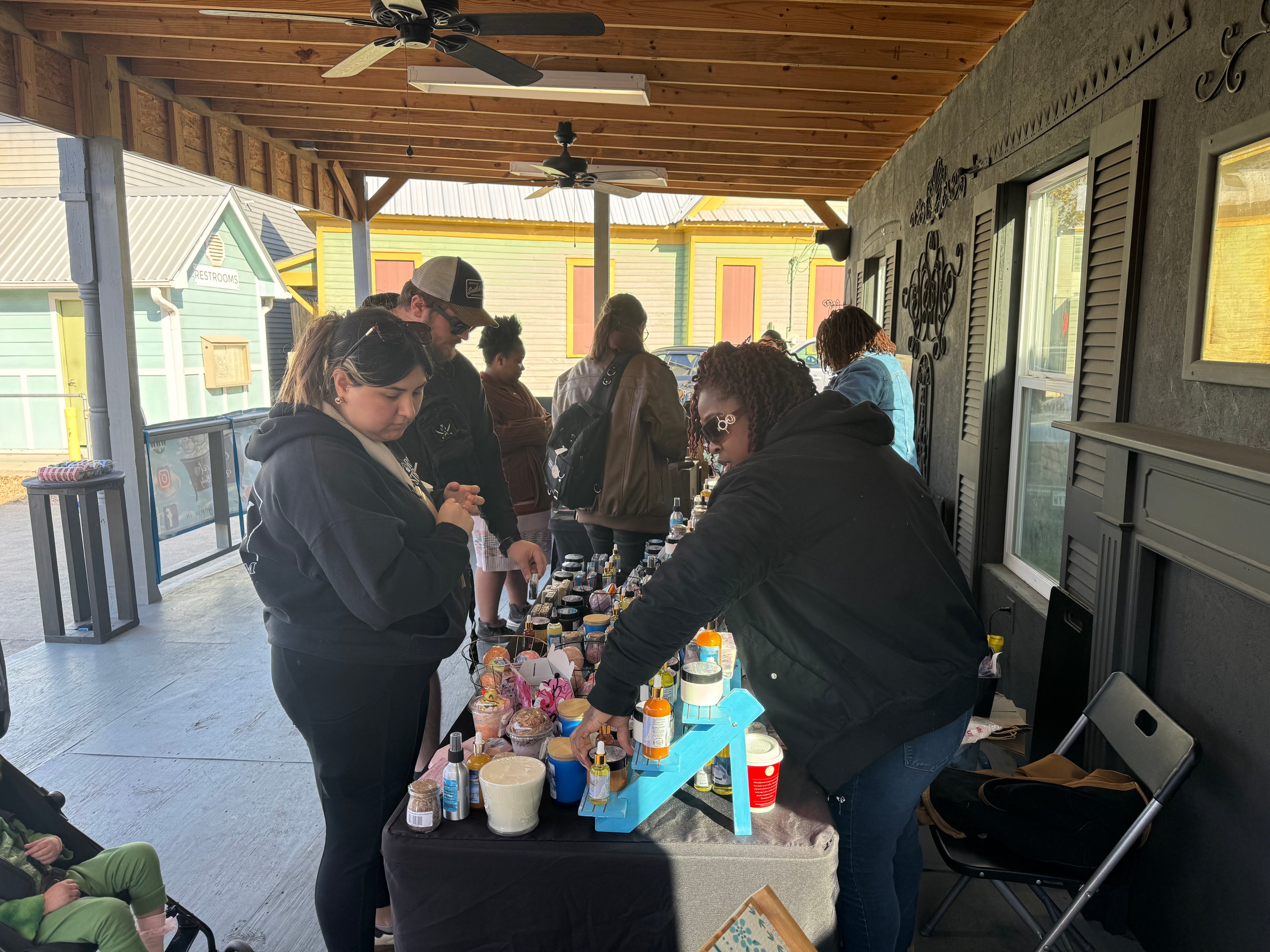 People gathered around a table with bath and body products on an outdoor patio.