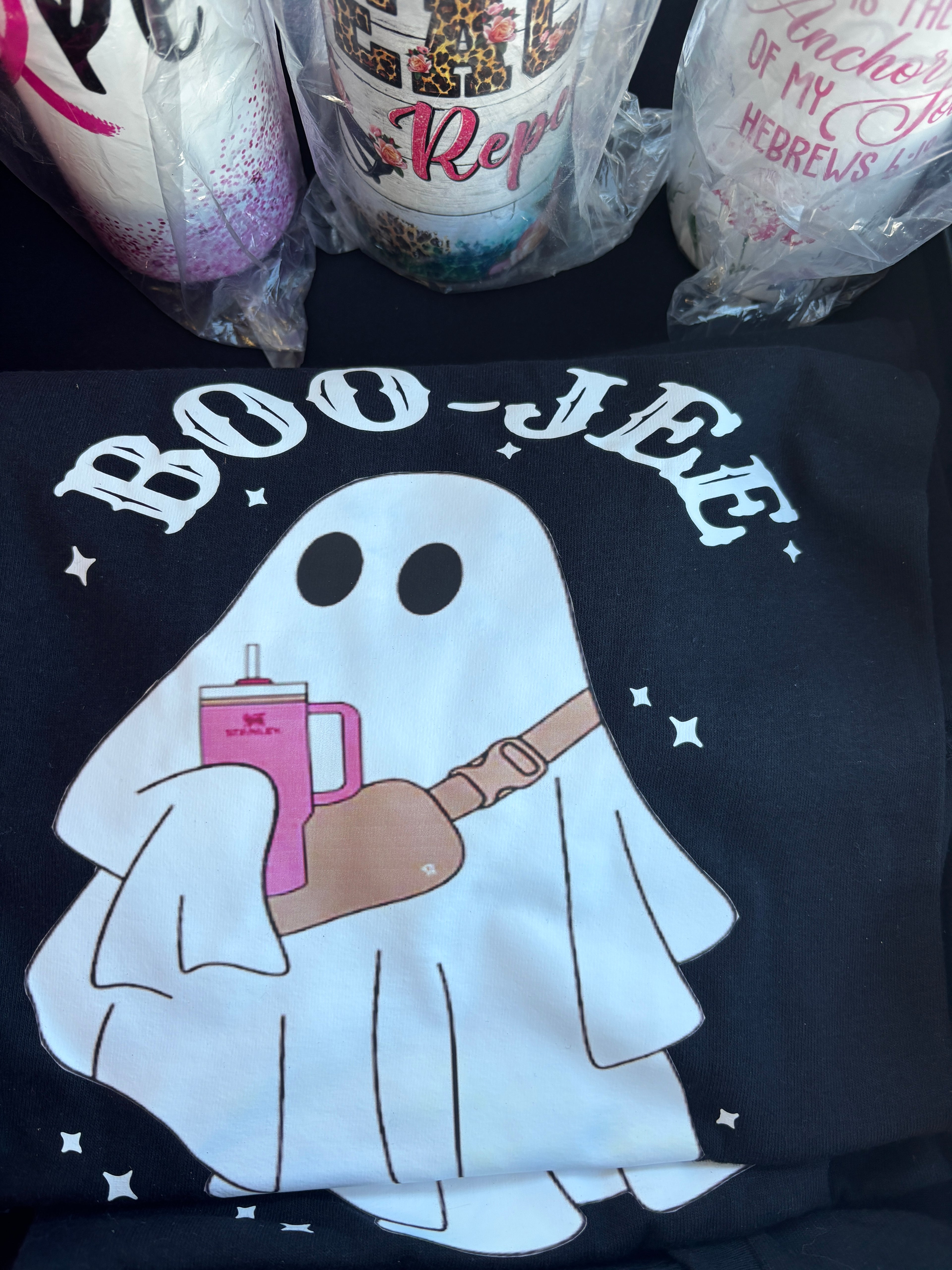 Black t-shirt with white graphic design featuring a skeleton hand holding a pink phone, text 'BOO-JEE' on a dark background.